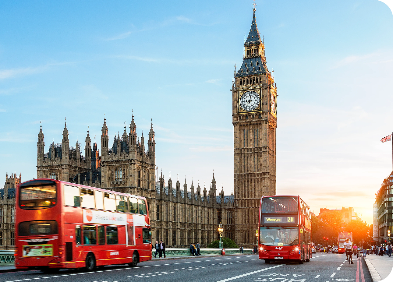Big Ben and red double-decker buses crossing Westminster Bridge at sunset